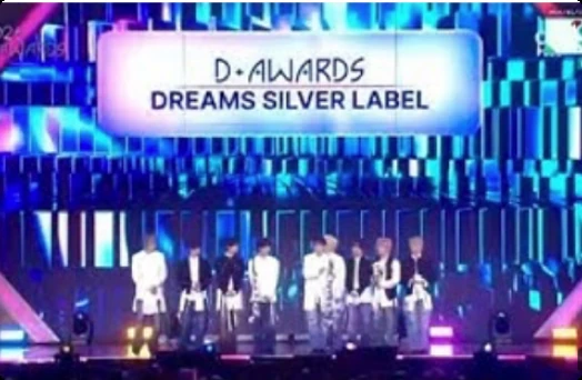 A group lined up on stage as the Dreams Silver Label award is announced on the screen behind them